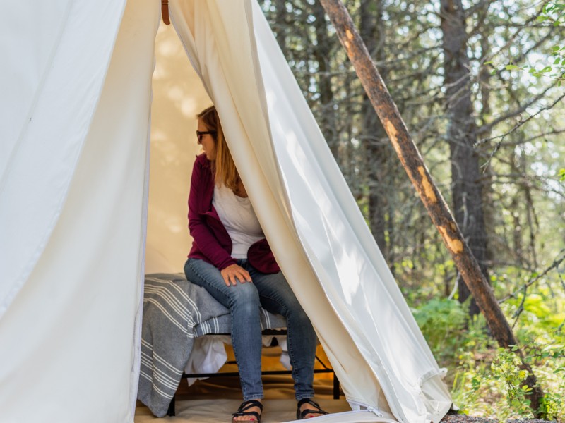 A person sitting on a bed in a tent by the woods