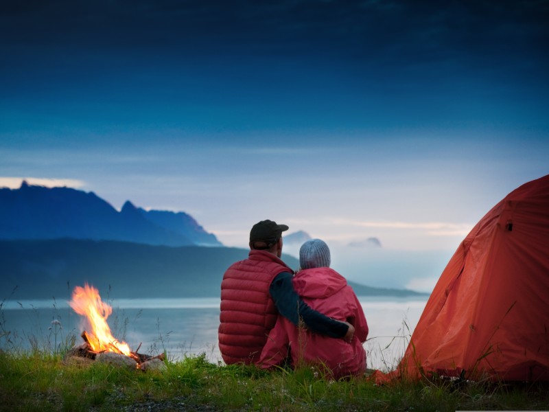 A couple camping by a lake with a campfire going