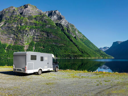 A camper parked by a lake facing the mountains