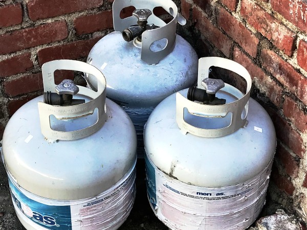 Three gas tanks next to a brick wall after being used