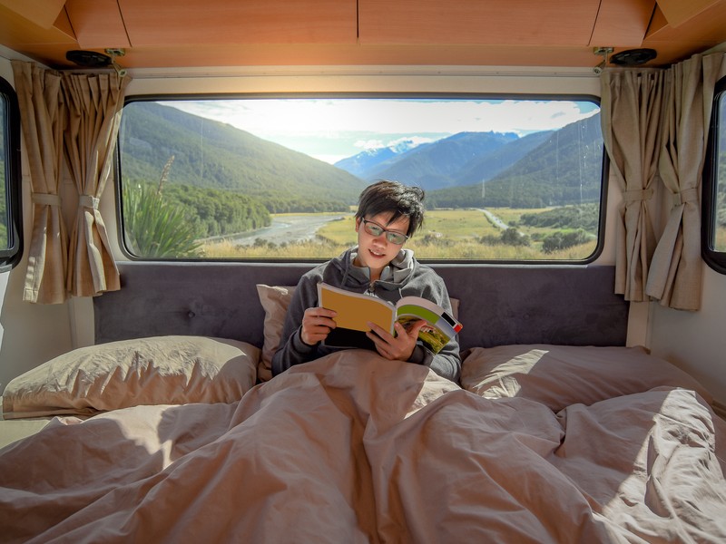 Someone reading in a camper with mountains in the background