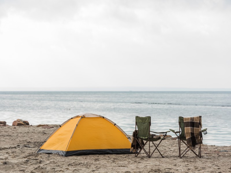 An orange tent on the beach with two chairs
